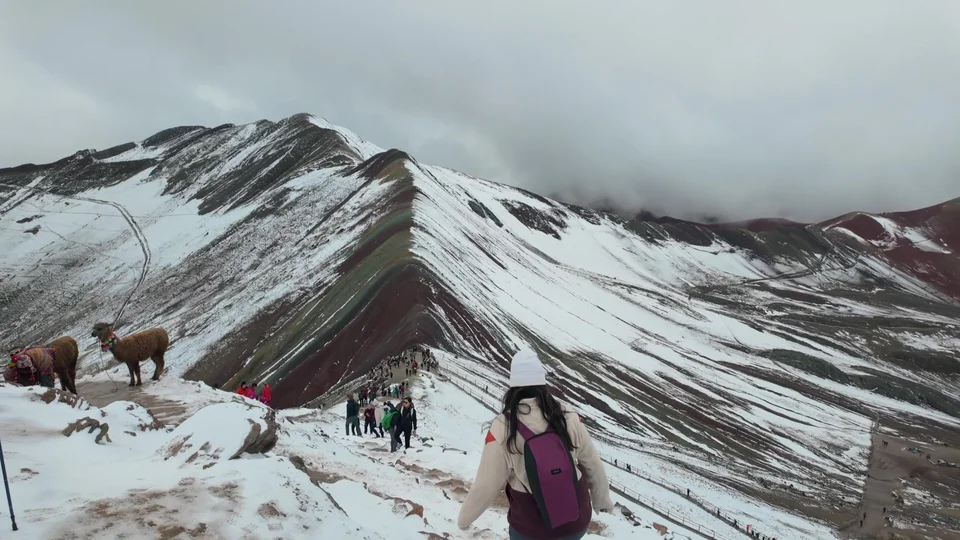 Hikers and llamas on the snow dusted ridge of Rainbow Mountain, Peru