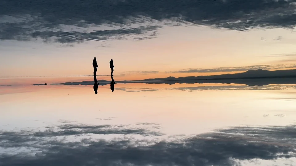 Two silhouettes reflected on the flooded Uyuni Salt Flats at sunrise