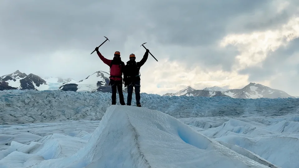Two hikers raising ice axes in celebration on top of the Grey Glacier